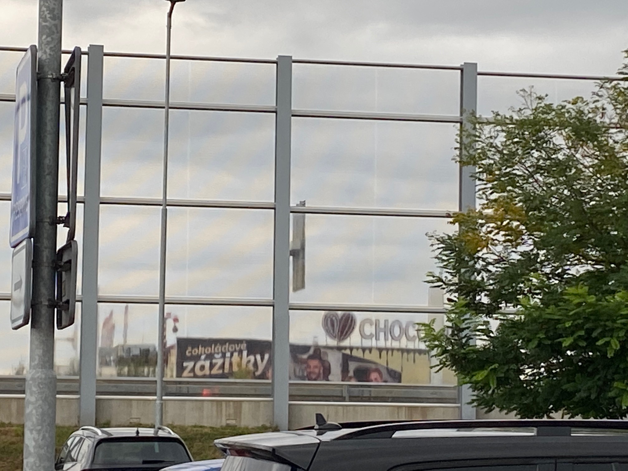 Hotová fasáda při pohledu od Lidlu přes protihlukovou stěnu. Viditelný zůstává její horní okraj se sdělením vlevo.